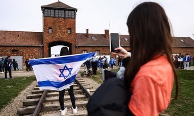 A person carries an Israeli flag in front of a brick building that is part of the former Auschwitz death camp
