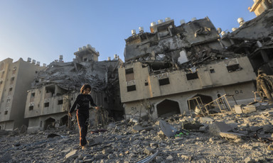 A girl with bare feet walks on debris-filled street next to bombed-out multi-story buildings