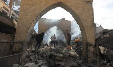 An angular arch frames men searching in the rubble, smoke rising from the ground