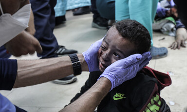 A doctor, wearing gloves, cradles the face of a small wounded child on the floor of a hospital 