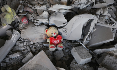 Amid the rubble osf a destroyed building is a stuffed teddy bear with a heart