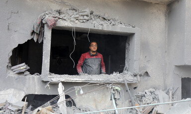 A man looks out from a glassless window of a destroyed home