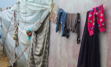 A woman smiles peeking her head out from a plastic tent, as clothing hangs on a line to dry