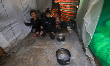 Three children sit beside pots in a makeshift tent 