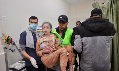 A medic wearing a yellow vest carries a girl who has been injured during Israel's war against Gaza