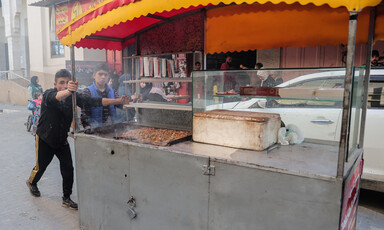 A boy pushes a food stall as another boy walks beside him 