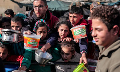 Children and some adults hold empty containers as the queue for food aid in Gaza