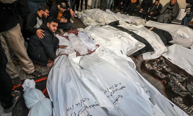 Men stand and sit around more than a dozen shrouded bodies, some of them small children