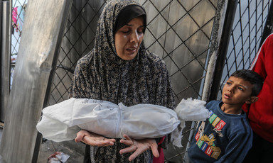 A woman cries while looking down at shrouded body of a small child in her arms as a young boy standing next to her looks towards her face