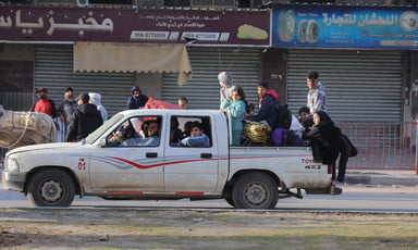 A four-door truck travels down the road, packed with people