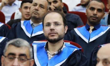 A man dressed in a graduation gown seated among others dressed the same way
