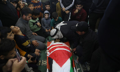 A man leans over and kisses the face of a man wrapped in a flag on a stretcher