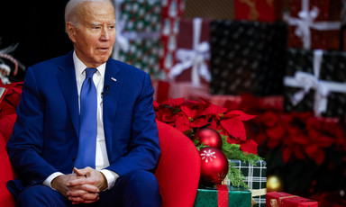 President Joe Biden sits in a red chair with wrapped boxes nearby