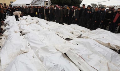 Men stand next to dozens of bodies wrrapped in white plastic