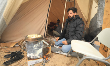 Outside of a tent, a man cooks bread on an outdoor stove