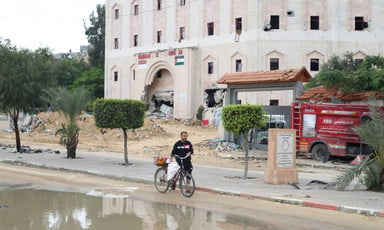 A man walks his bike in front of the wrecked facade of the Indonesian Hospital