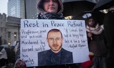 A protester holds a placard with a portrait of Refaat Alareer and a quote from his if I must die poem