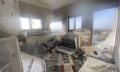 A severely damanged kitchen with shattered windows, destroyed walls and a tossed-over stove