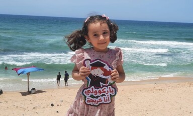 Smiling Kenzi al-Madoun, 5 years old, poses on the beach after kindergarten graduation