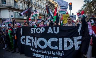 People carry black banner with white text reading Stop Au Genocide and Palestine flags