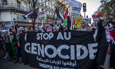 People carry black banner with white text reading Stop Au Genocide and Palestine flags