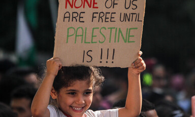 A child carries a sign that reads: None of us are free until Palestine is