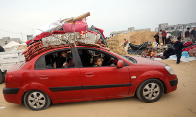 Palestinians in a red car loaded on top with mattresses and other supplies