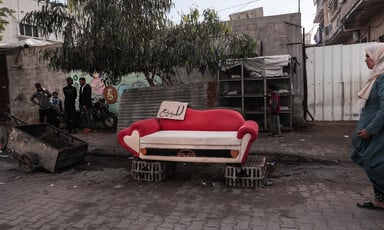 A red and white couch with heart design on the street, with a for-sale sign in Arabic