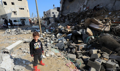 A young boy in a Star Wars sweatshirt stands next to a destroyed building