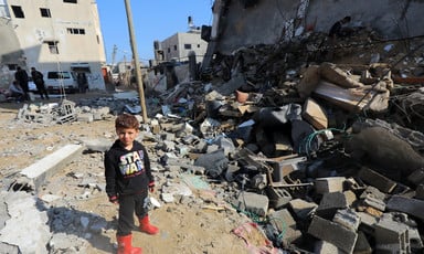 A young boy in a Star Wars sweatshirt stands next to a destroyed building