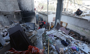 A few people gather beside a building which has been destroyed by Gaza 