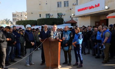 A man from the World Health Organization stands at a podium behind the Emergency sign of a Gaza hospital