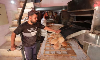 A baker removes loaves of flat bread from the oven