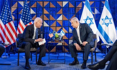 Joe Biden and Benjamin Netanyahu, both seated, lean toward each other with American and Israeli flags behind them
