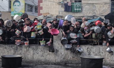 People stand behind a short wall, holding containers to collect food 