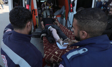 Palestinian medics wearing dark blue uniforms beside a man on a stretcher who is being taken out of an ambulance