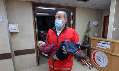 A medic wearing a mask carries an injured child in Gaza 