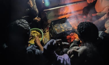 At night, a close-up of an outdoor fire and a meal being prepared by hand