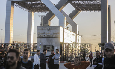 A number of men gather around a structure with the words Rafah Crossing Point written on it
