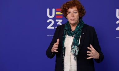 Belgian Deputy Prime Minister Petra De Sutter makes hands gestures in front of a blue backdrop 