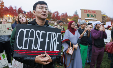 Close-up of a man holding a sign reading "ceasefire" standing on lawn with several other people