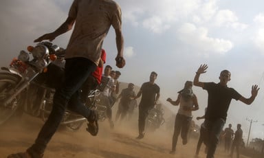A ground view of individuals running as dirt flies in the air.