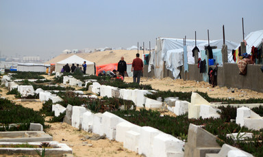 Men walk past a cemetery and tents. 