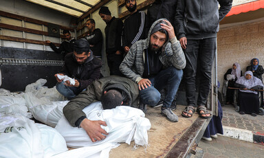 Two young men kneel next to shrouded bodies while a third leans onto and embraces a shrouded body
