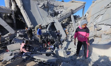 A girl stands in the foreground of a group of people on top of the rubble of a destroyed building