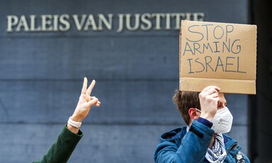 Man holds sign saying stop arming Israel outside court building while another person makes victory sign