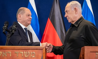 Scholz and Netanyahu shake hands by podiums with Israeli and German flags behind