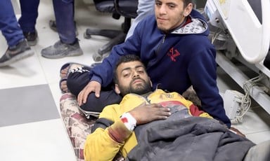 One man lies on a stretcher and another man sits beside him in a Gaza City hospital 
