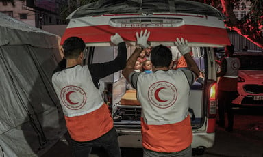 Two medics wearing vests with the logo of the Palestine Red Crescent Society prepare to close an ambulance door 