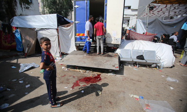 A young boy stands next to a blood stain on pavement and a truck being unloaded.